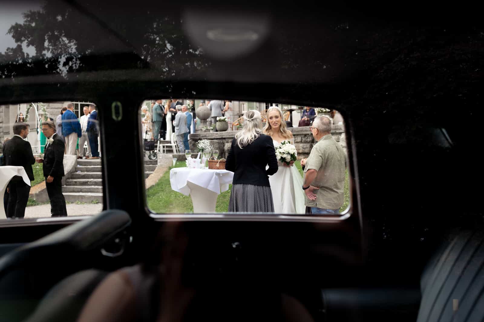 Braut mit Brautstrauß durch Vintage-Autofenster während Cocktailstunde fotografiert