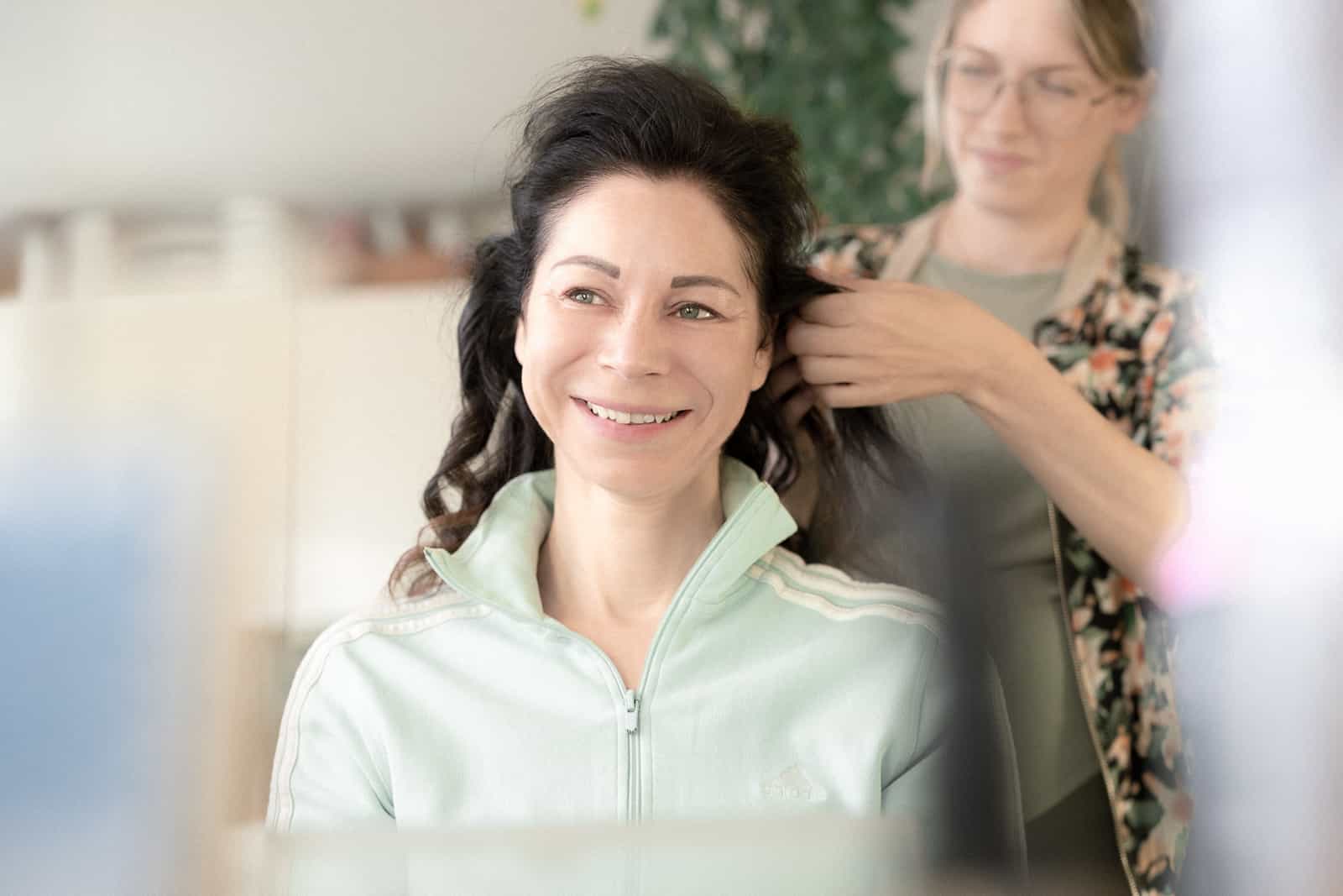 Lachende Braut in Jacke während Haarstyling