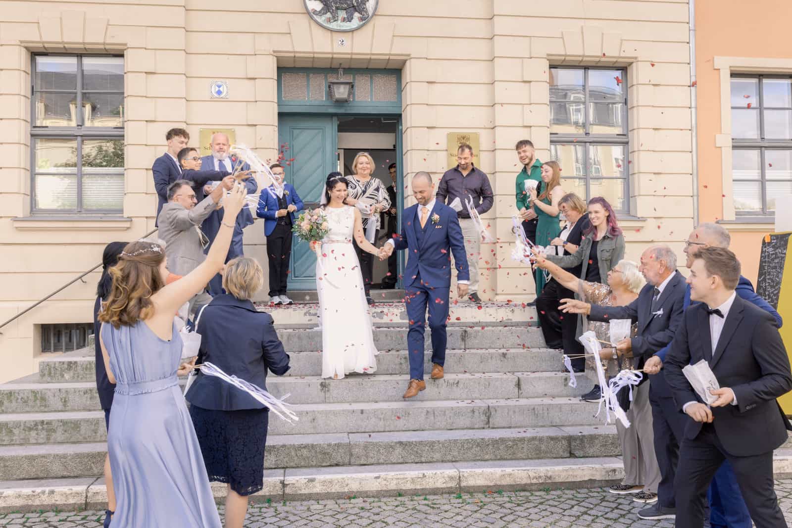 Brautpaar verlässt Rathaus unter Konfetti mit jubelnden Gästen auf Treppe