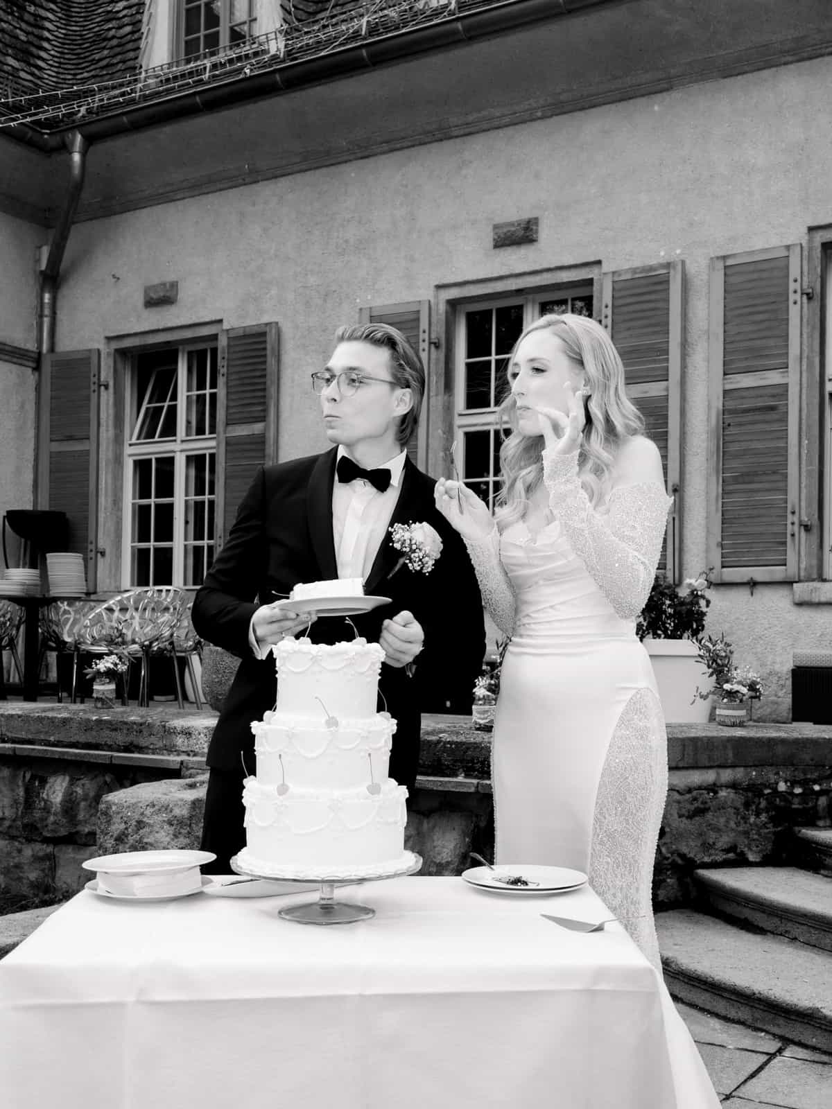 Braut probiert Hochzeitstorte während Bräutigam zuschaut, schwarz-weiß Aufnahme im Schlosshof Kartzow
