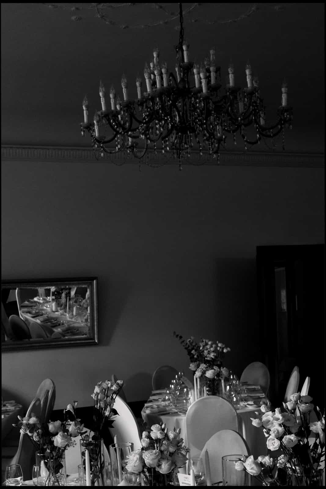 Elegante Hochzeitstafel mit weißen Rosen und Kristallleuchter im historischen Festsaal, Schwarzweiß