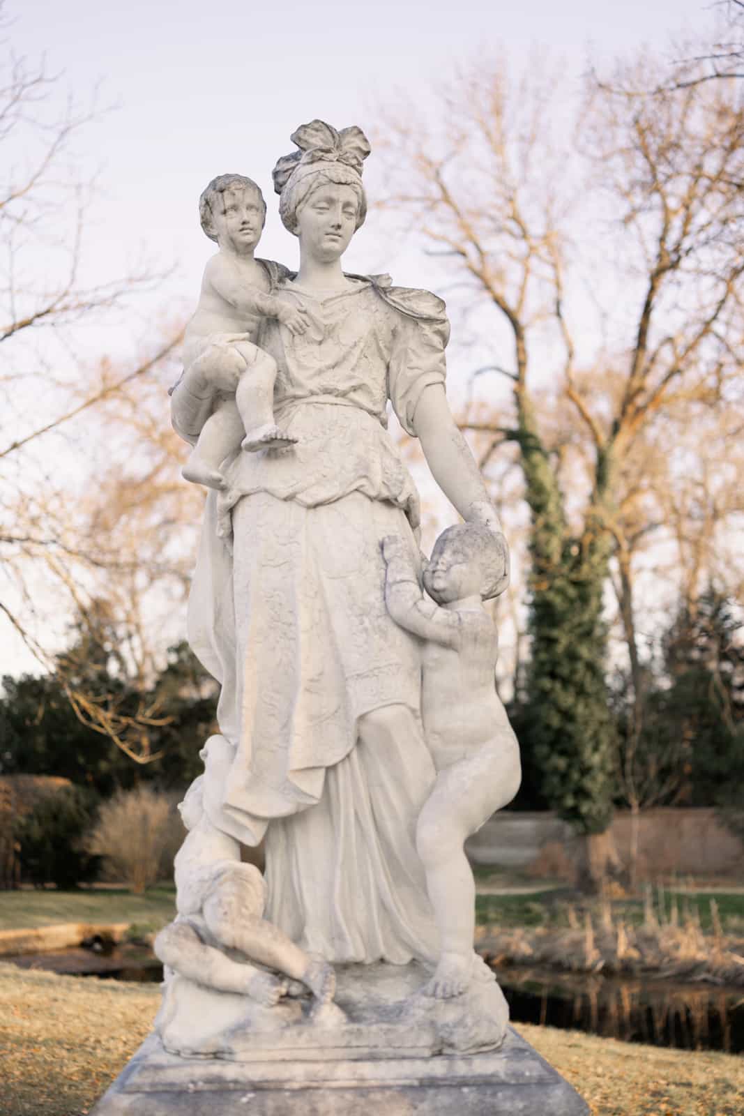 Barocke Gartenstatue mit Putten vor kahlen Bäumen im Schlosspark