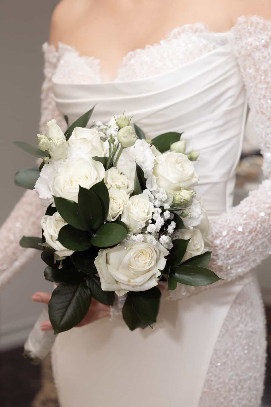 Bride in white satin dress with lace sleeves holding bouquet of white roses