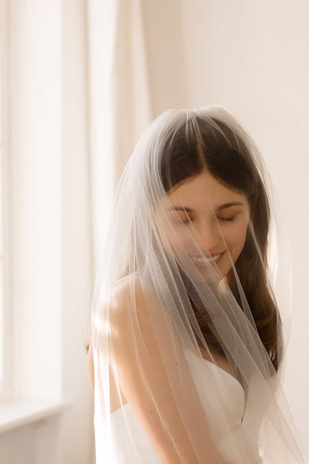 Bride with closed eyes and gentle smile under veil, soft backlight