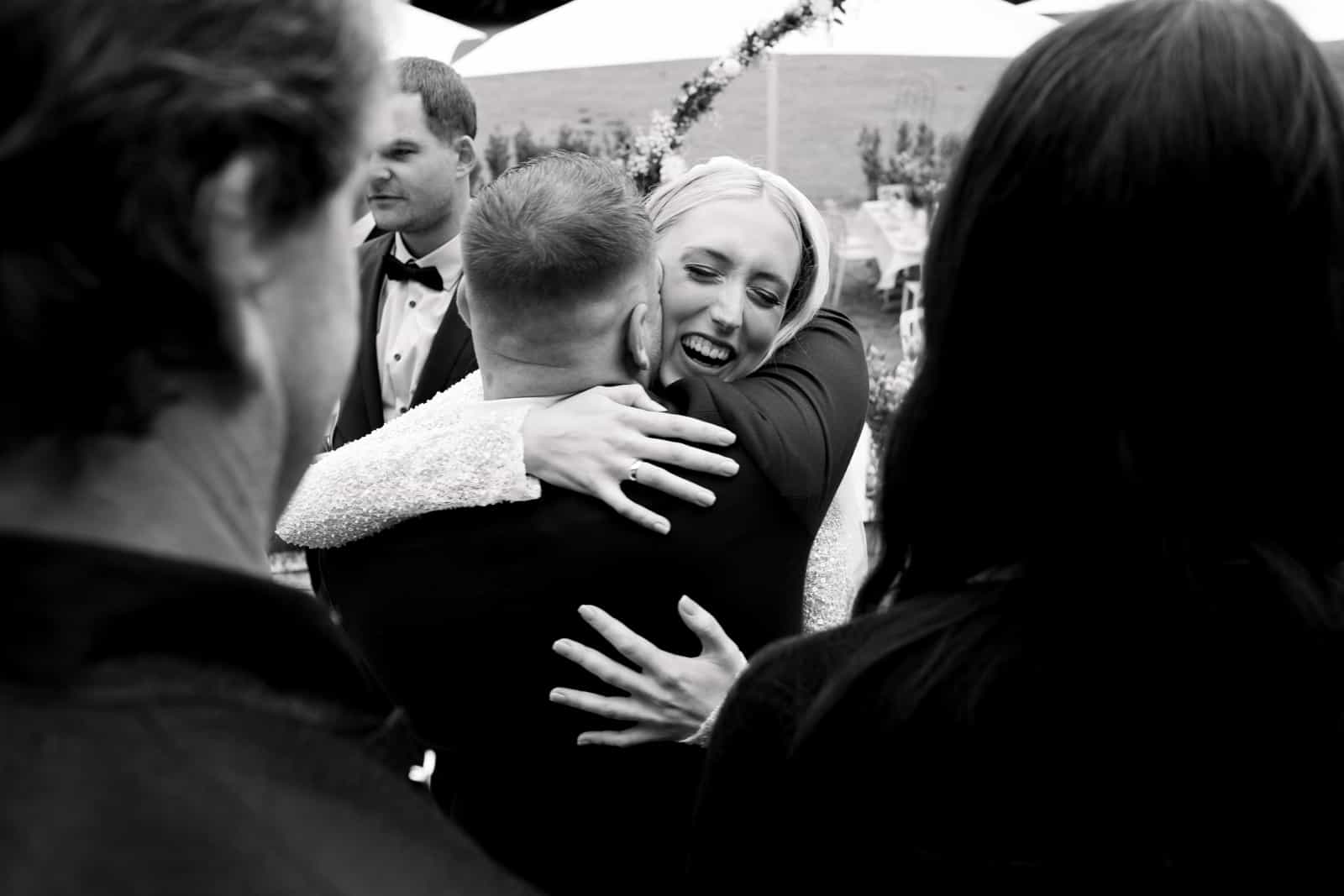 Bride embracing guest during congratulations after ceremony with radiant smile, black and white