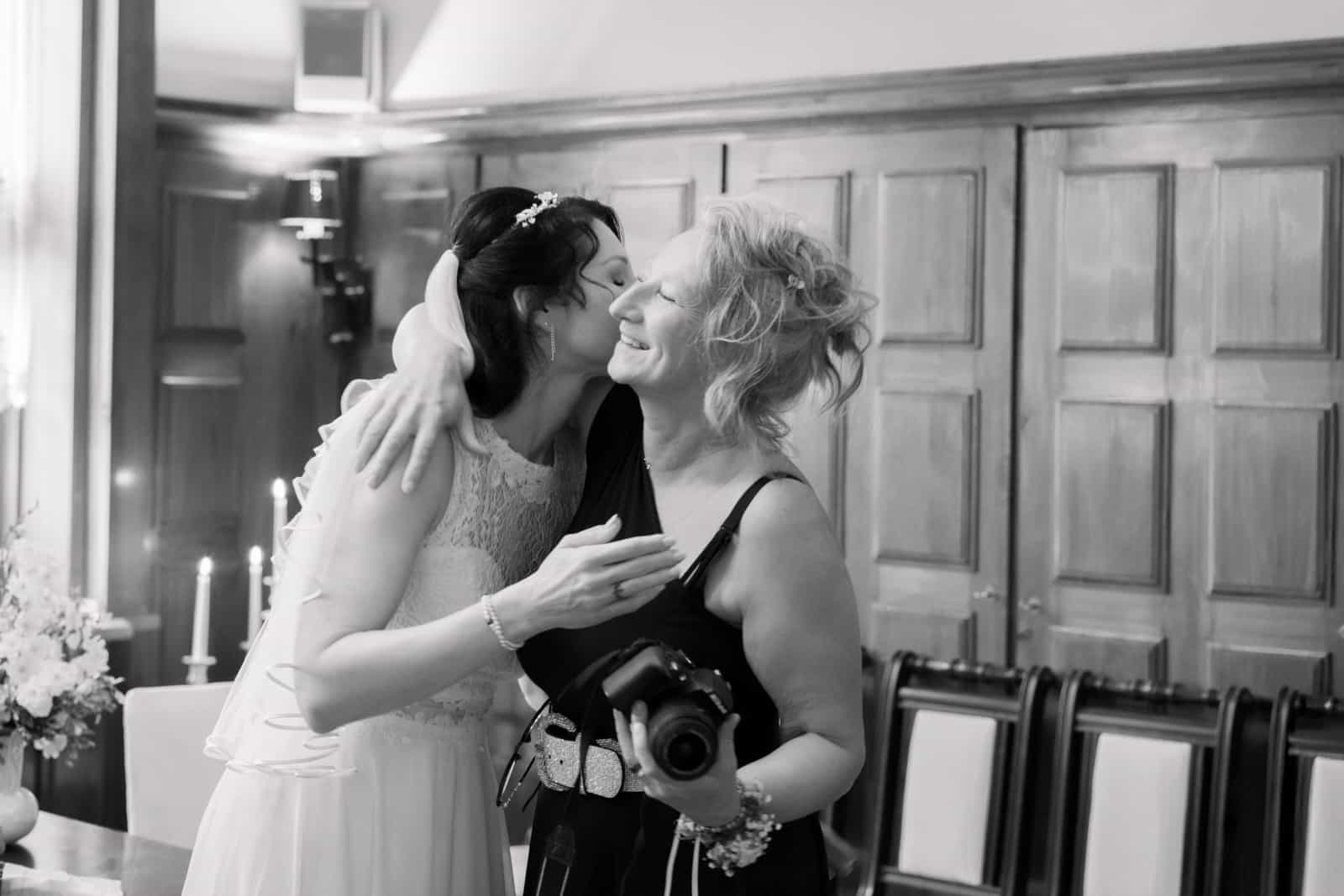 Bride embracing photographer with camera in wood-paneled room, black and white