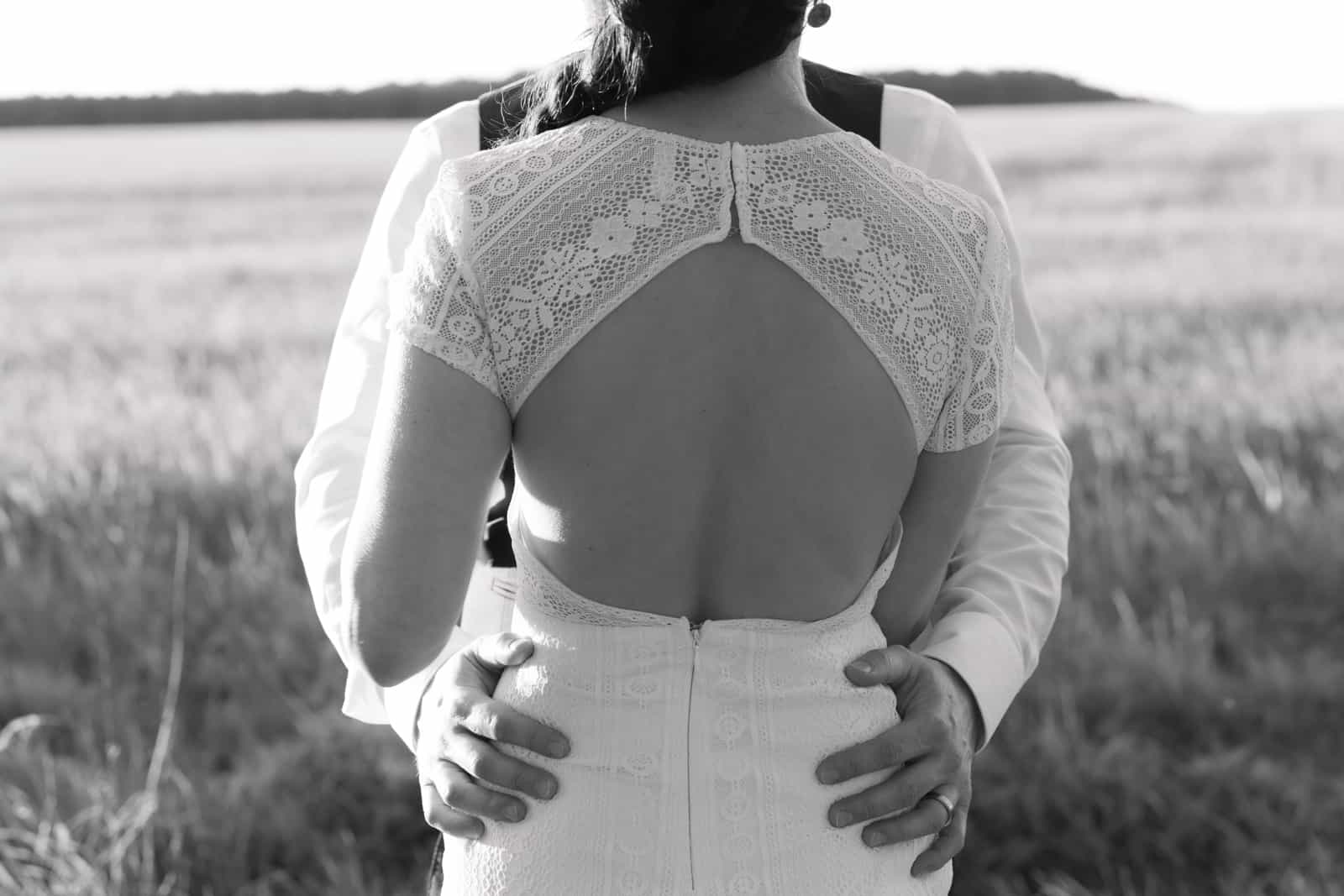 Bride and groom embracing photographed from behind in a cornfield, bride wearing dress with lace details, Brandenburg wedding photography