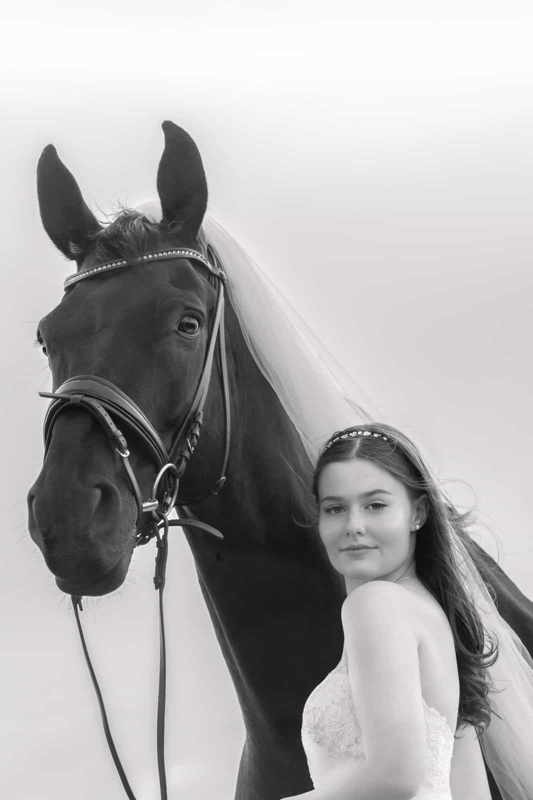 Bride with tiara beside black horse, both looking at camera, black and white