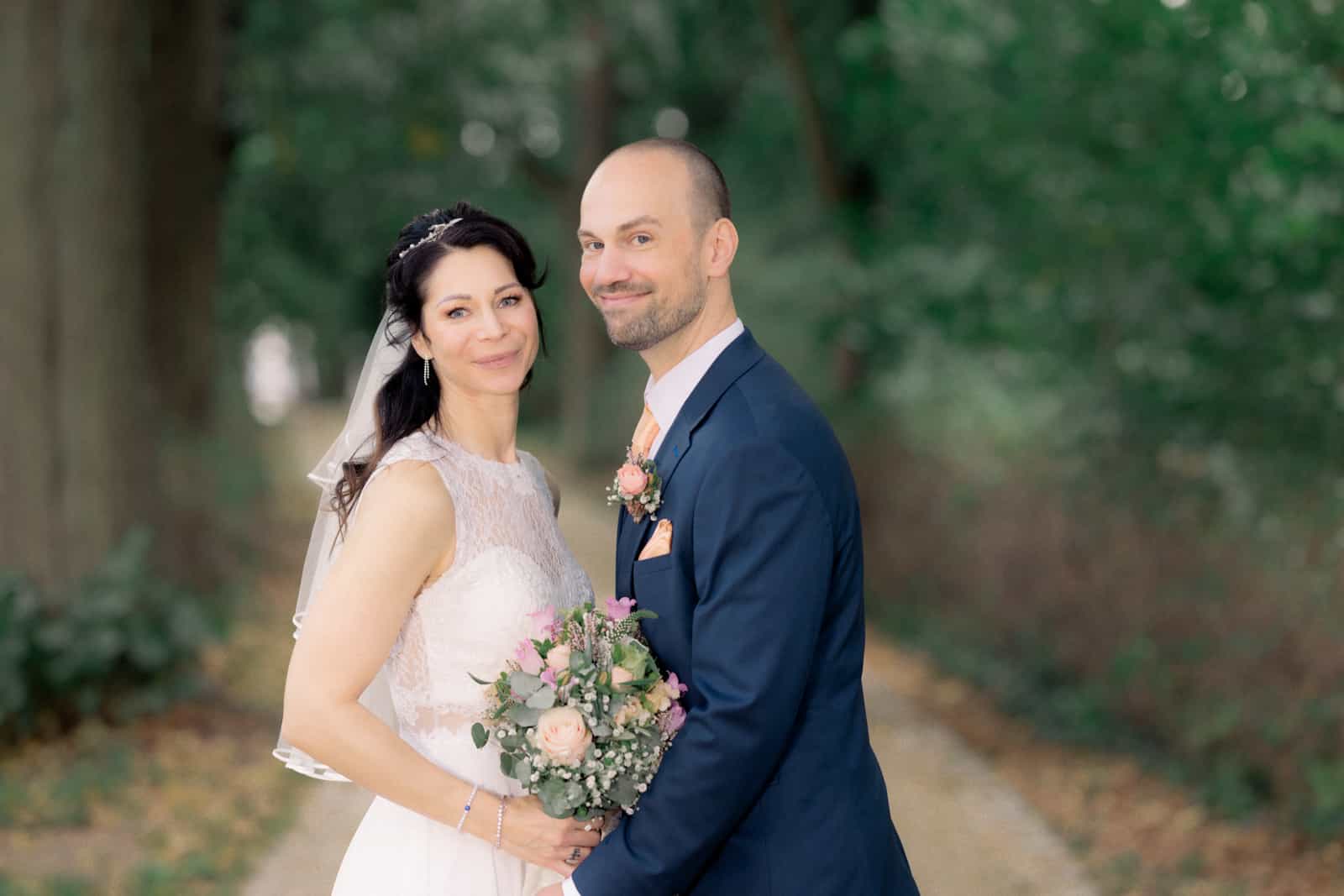 Bride with veil and rose bouquet laughing at groom, green background
