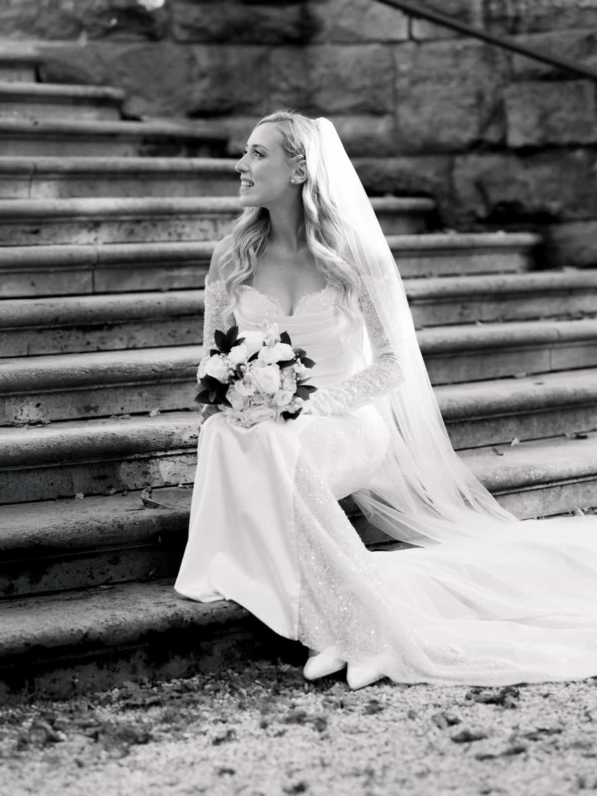 Bride in elegant lace dress with veil and bouquet on stone stairs - Schloss Kartzow wedding photography