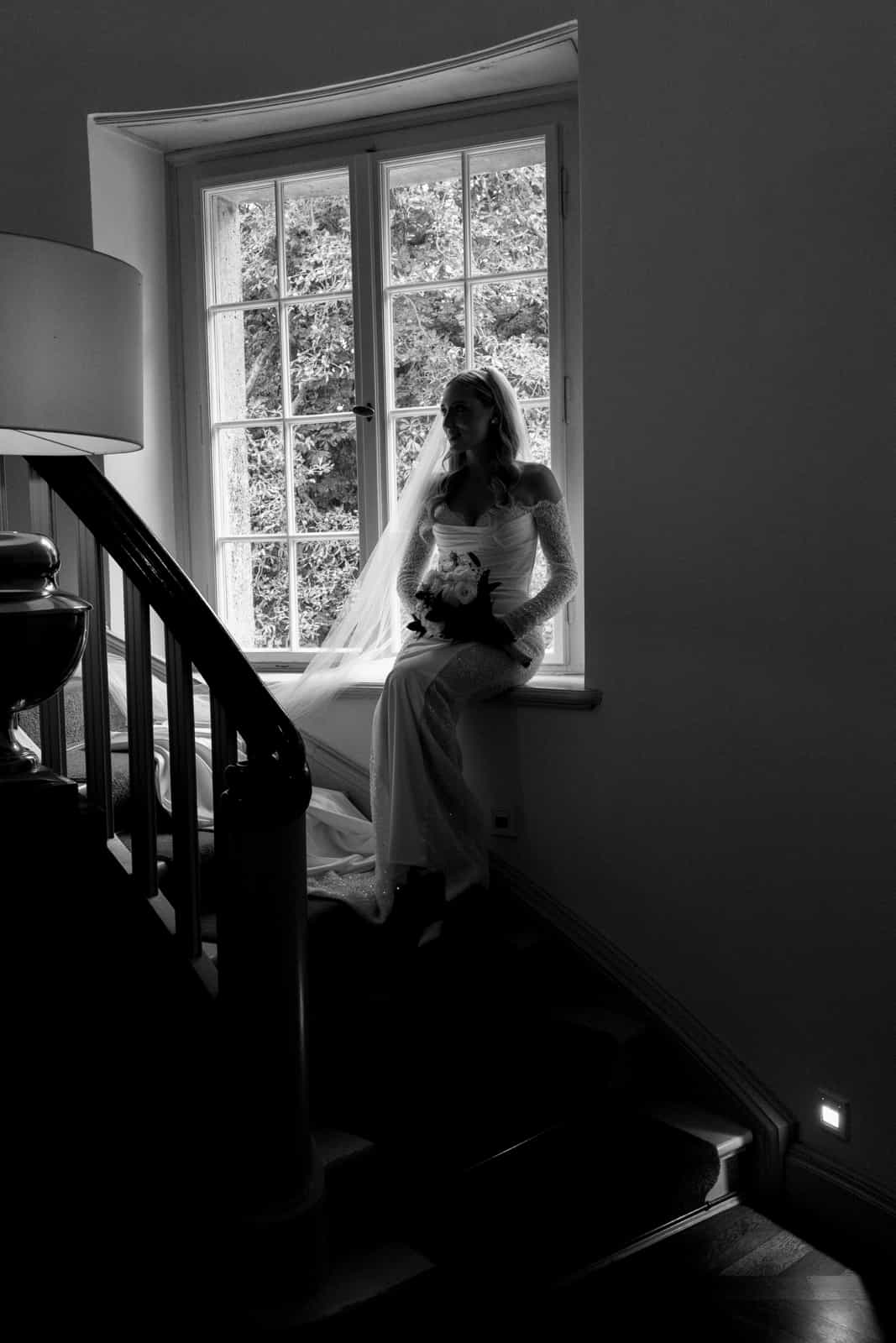 Dramatic silhouette of bride at window with veil and bouquet, black and white