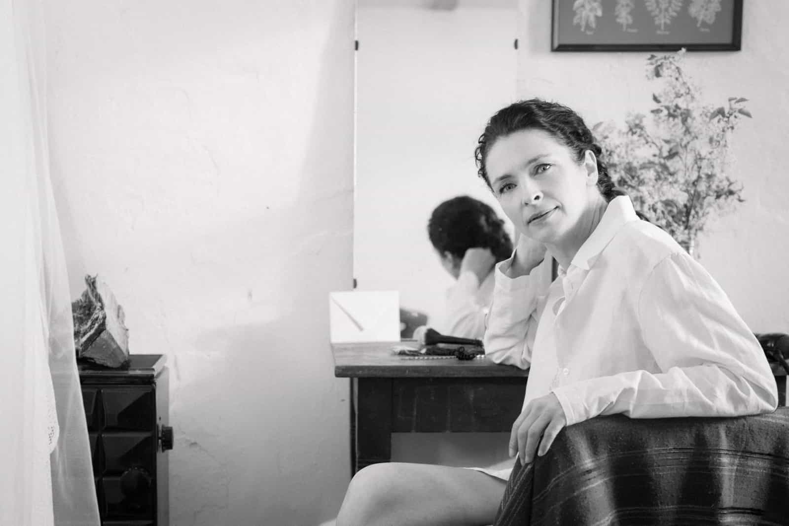 Woman in white blouse at rustic vanity table with mirror, black and white