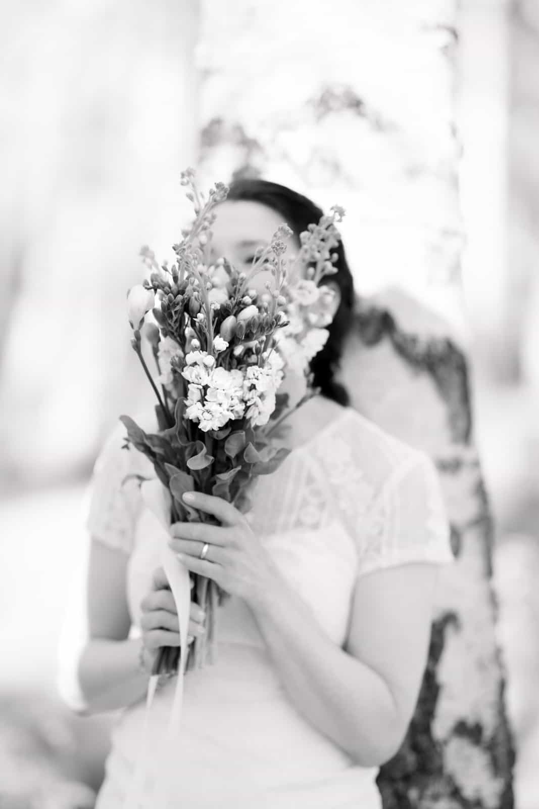 Bride with wildflower bouquet in front of face in birch forest, black and white