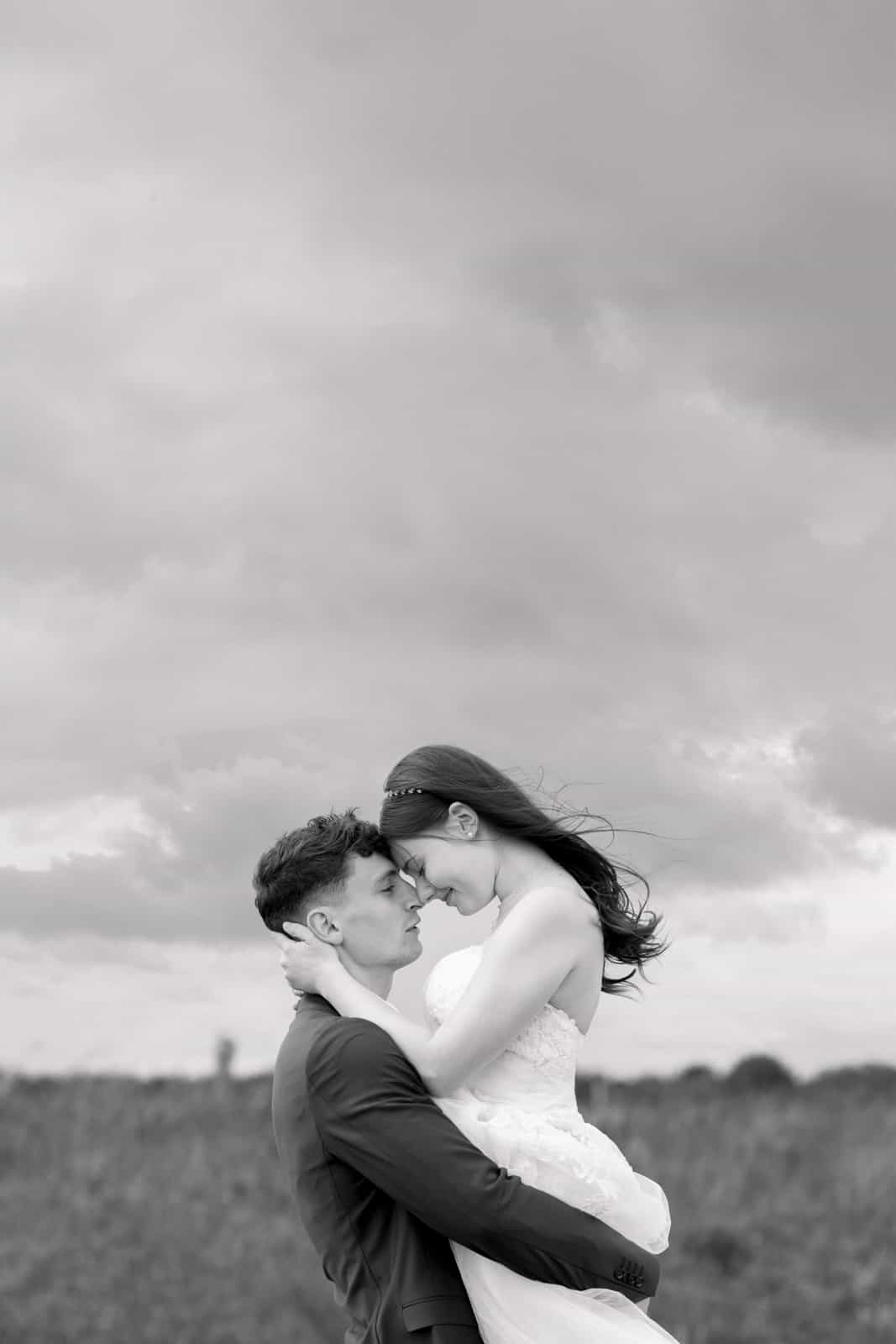 Couple forehead to forehead with dramatic sky in background, black and white