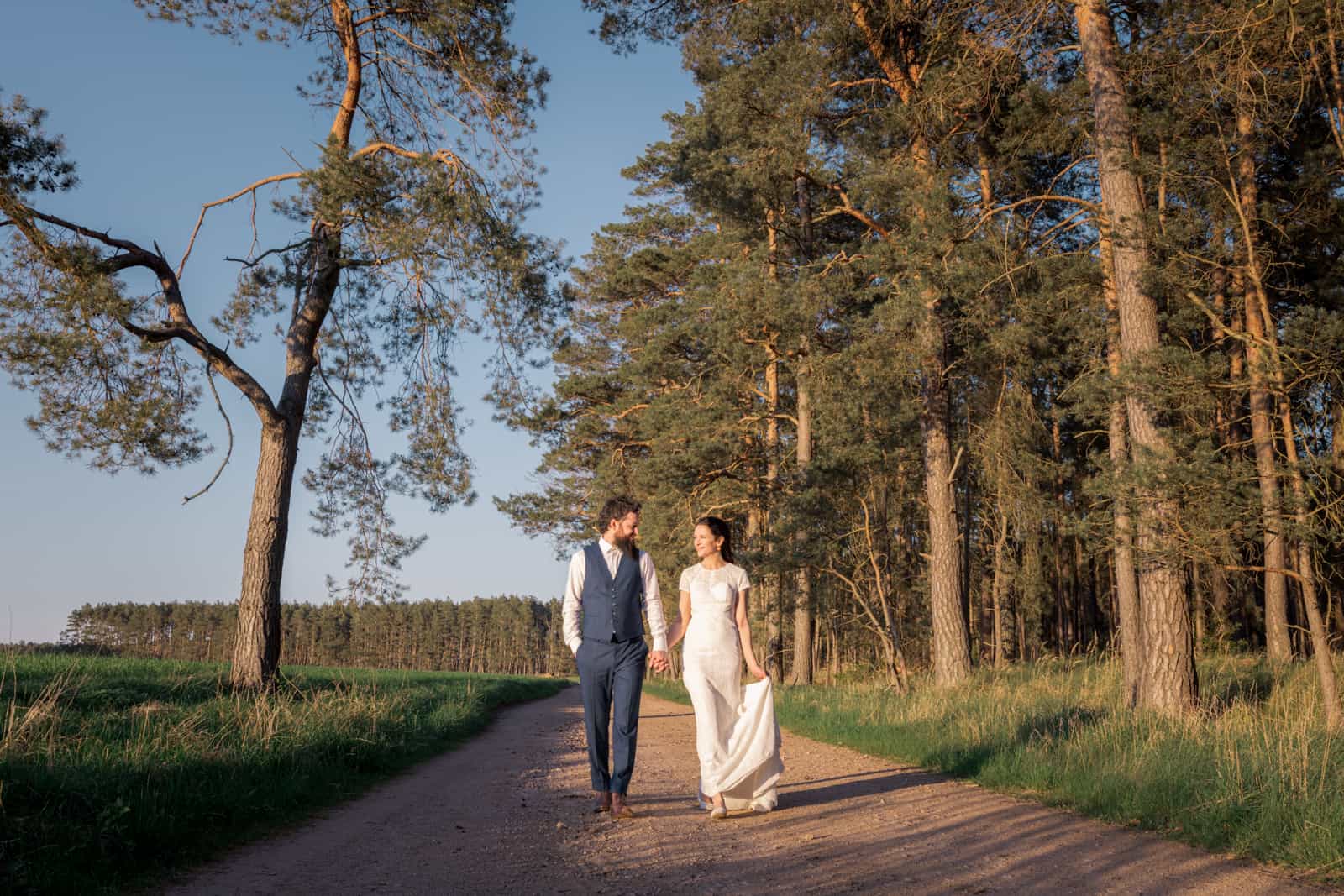 Couple walking hand in hand on country path at golden hour with pine trees