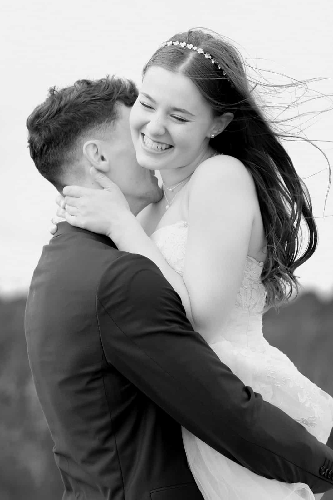 Couple in intimate embrace, bride laughing with windswept hair, black and white