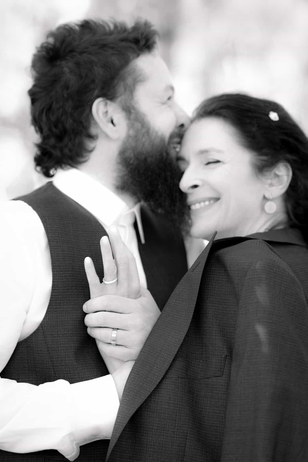 Intimate embrace with bride's hand and wedding ring on groom's vest, black and white