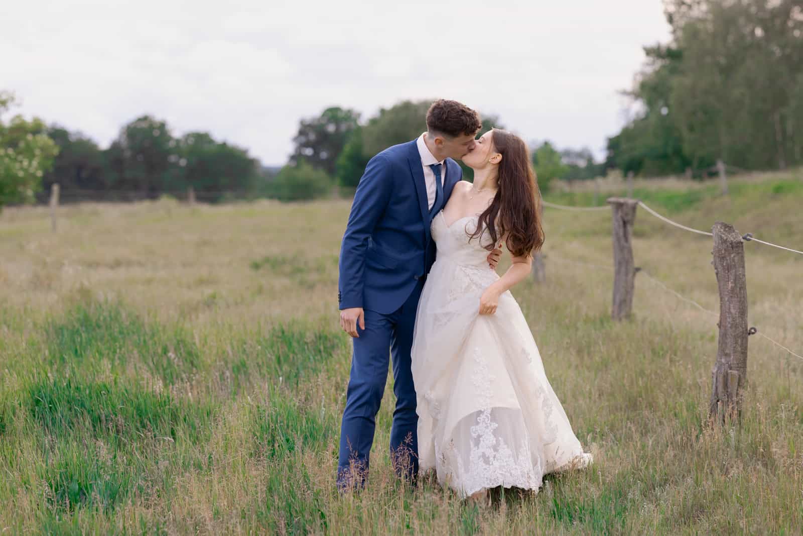 Couple kissing in meadow with wooden fence and trees in background
