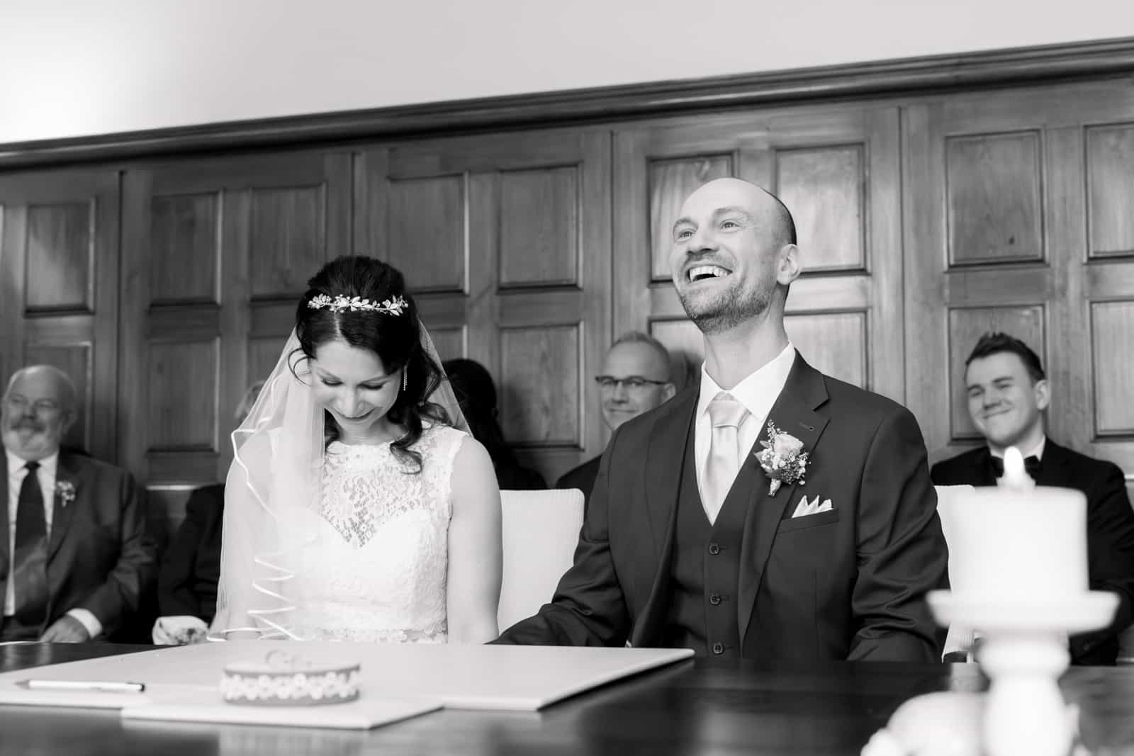 Couple laughing during civil ceremony in wood-paneled room, black and white