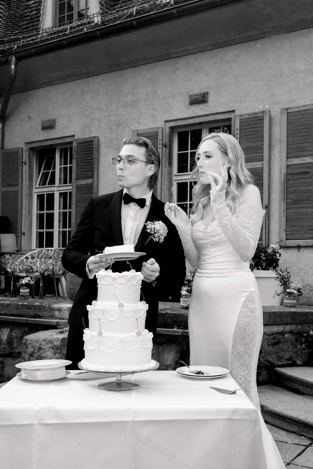 Couple playfully tasting wedding cake in front of castle backdrop, black and white
