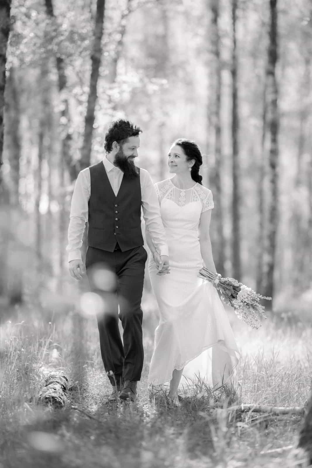 Couple walking hand in hand through birch forest, looking at each other, black and white