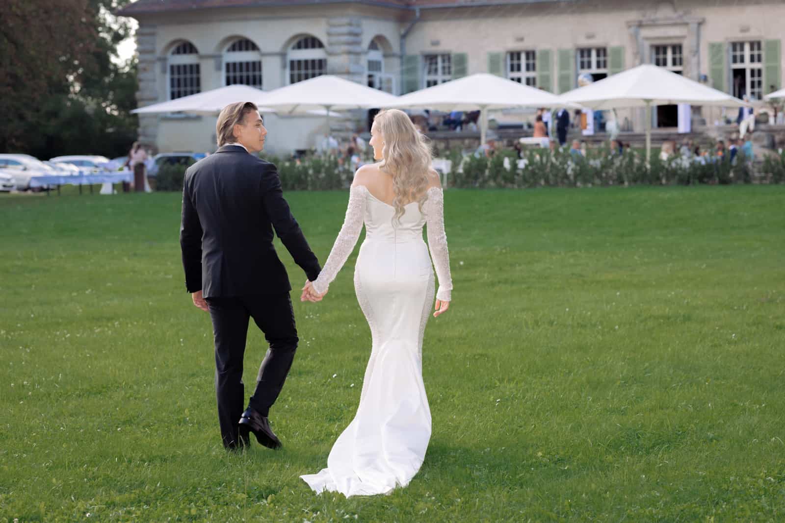 Couple walking from behind toward manor house across green lawn with train