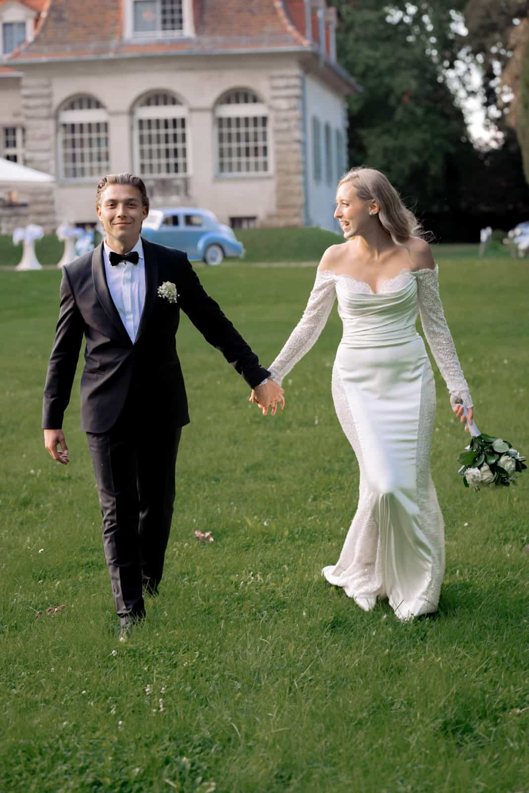 Couple holding hands with vintage car and manor house in background