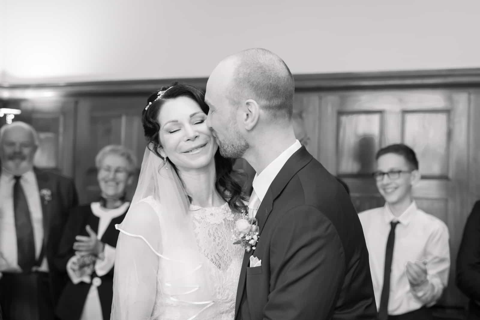 Groom kissing bride after ceremony while guests applaud, black and white