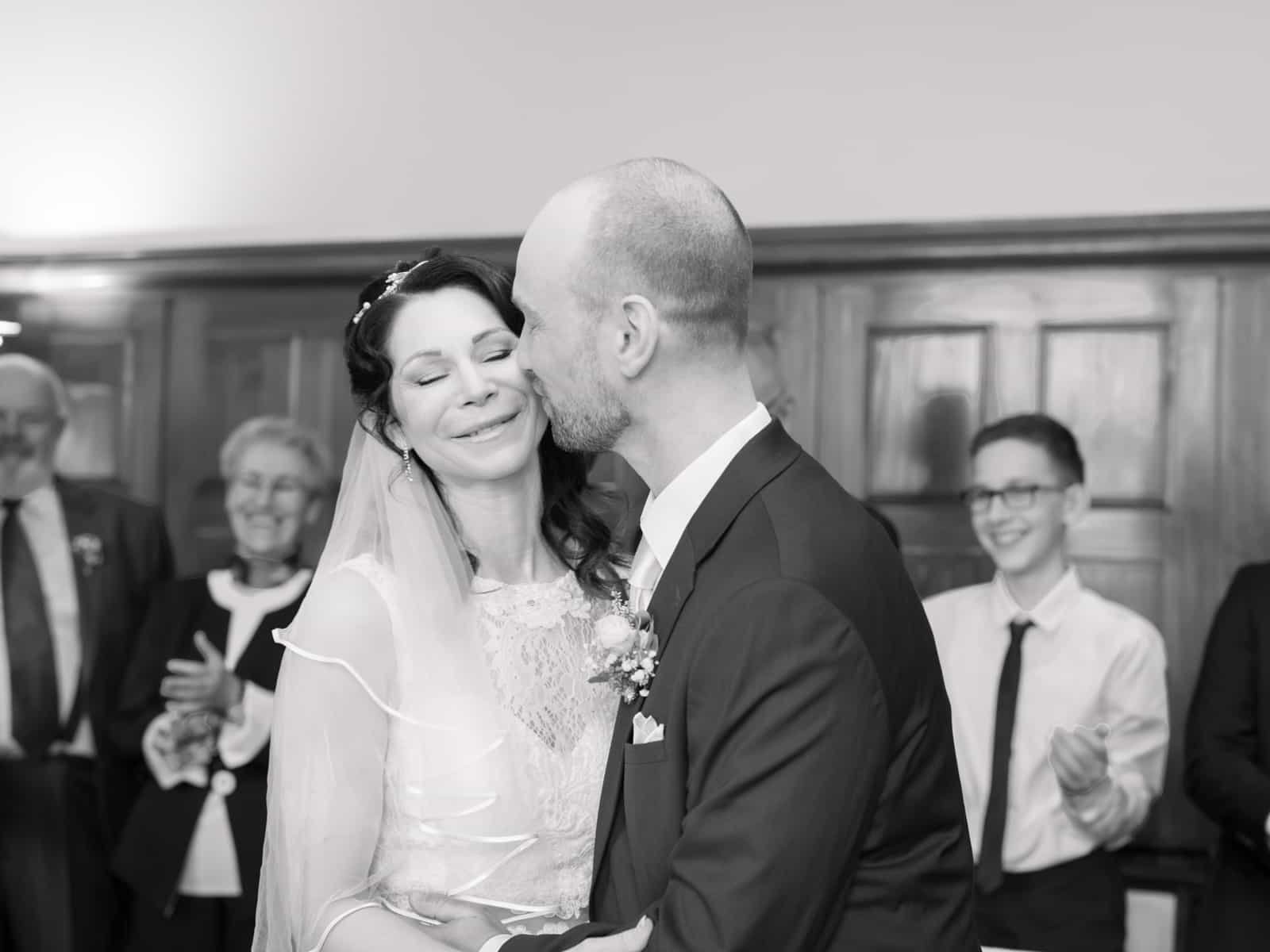 Groom kissing bride on cheek after ceremony with applauding guests