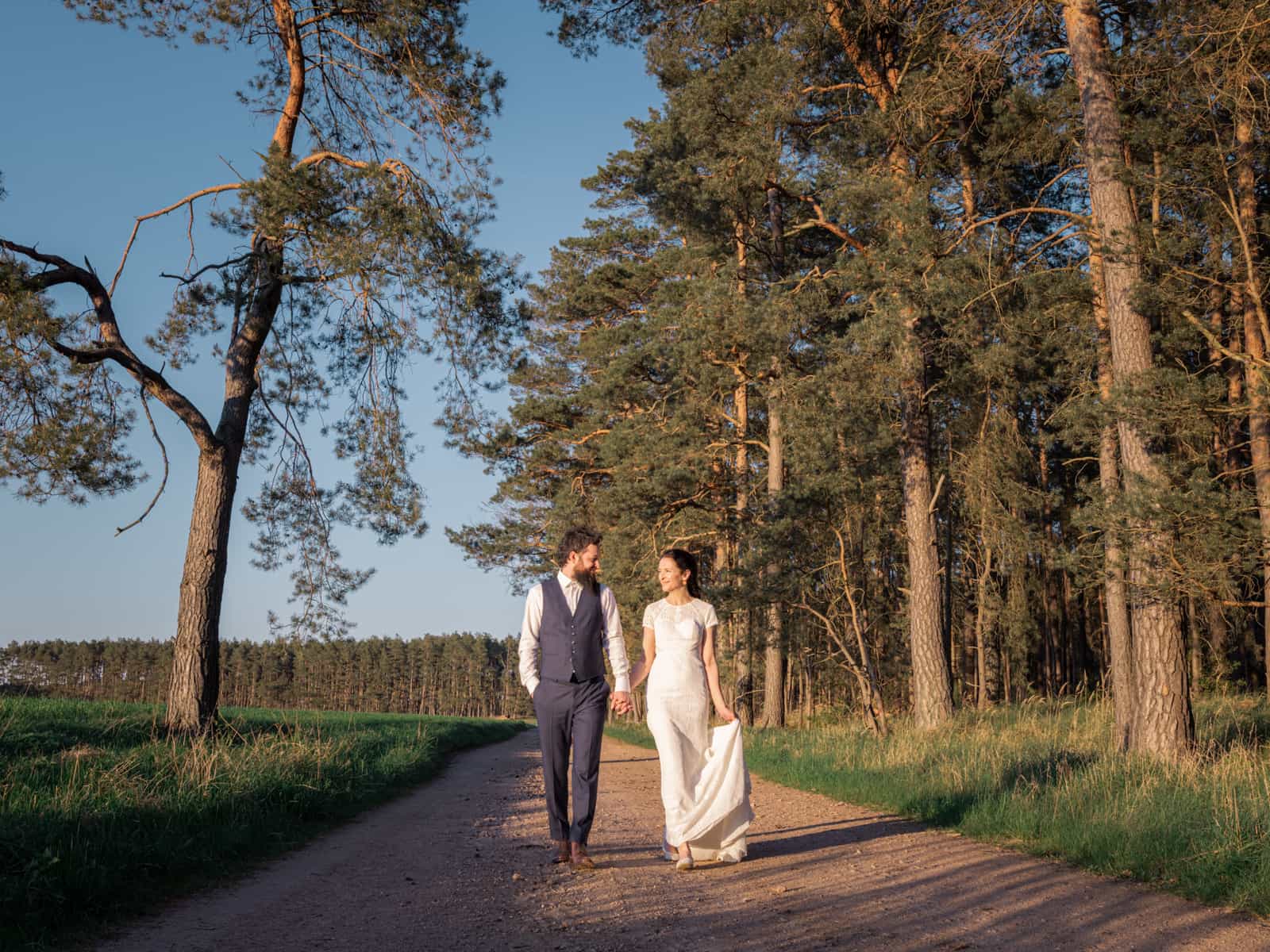 Couple walking hand in hand on field path at golden sunset