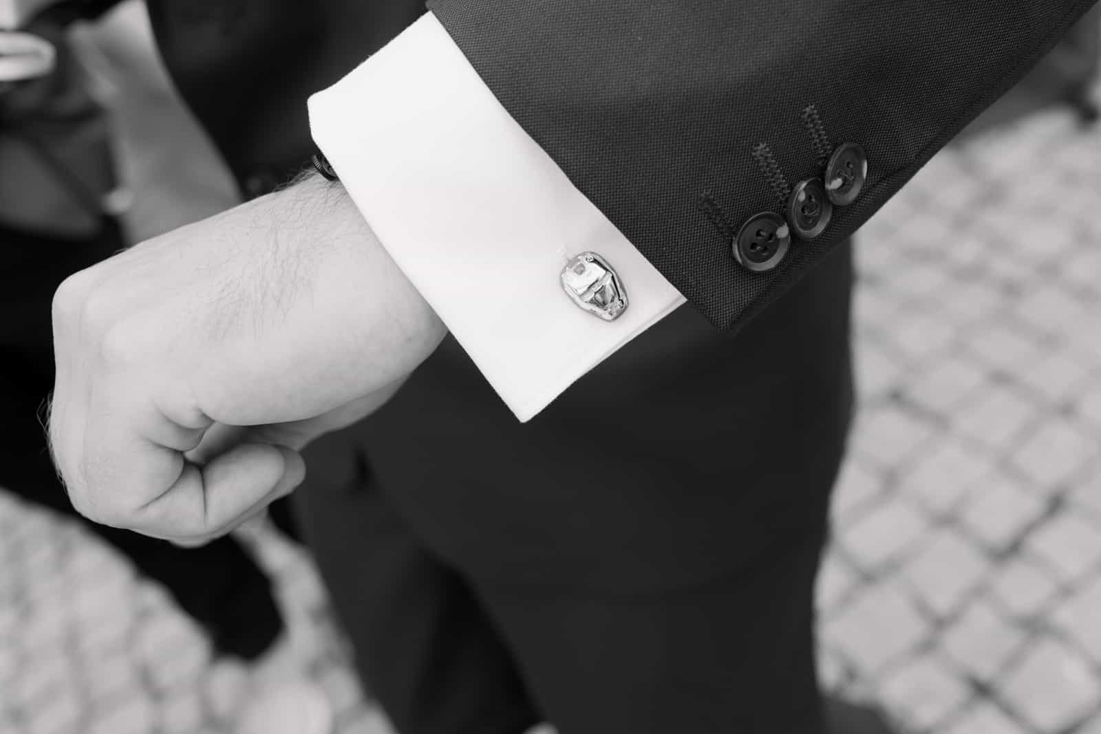 Silver car-shaped cufflink on groom's white shirt cuff, black and white