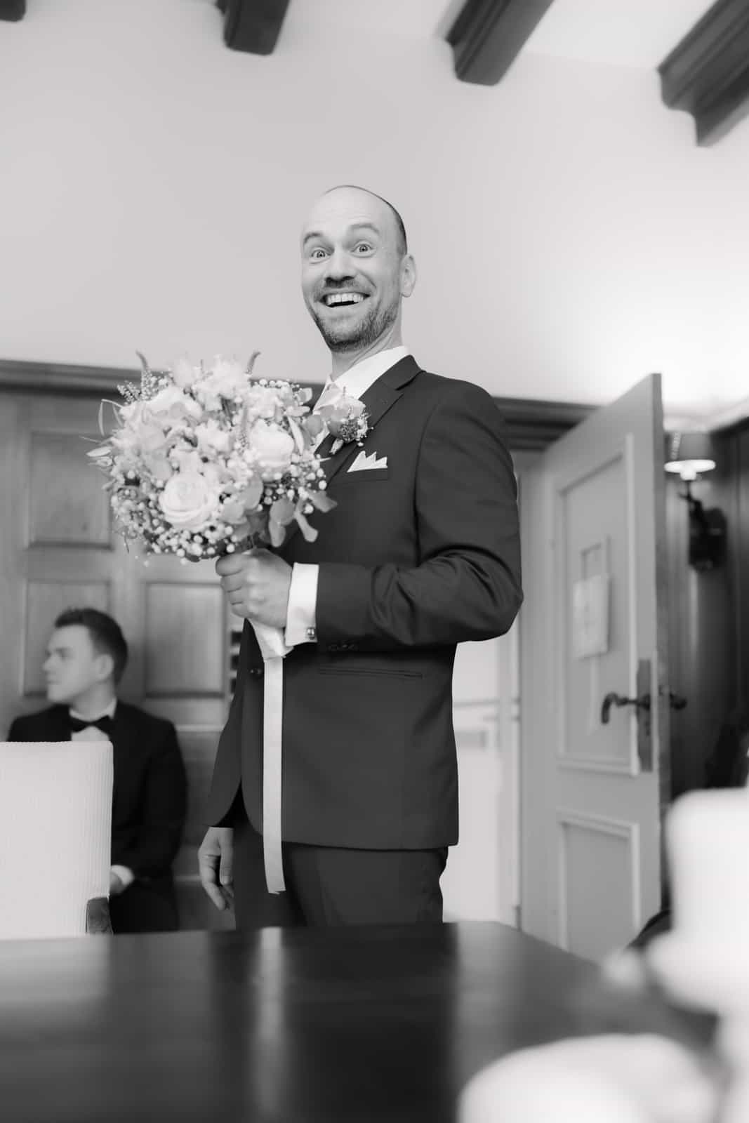 Groom with surprised face holding rose bouquet, black and white