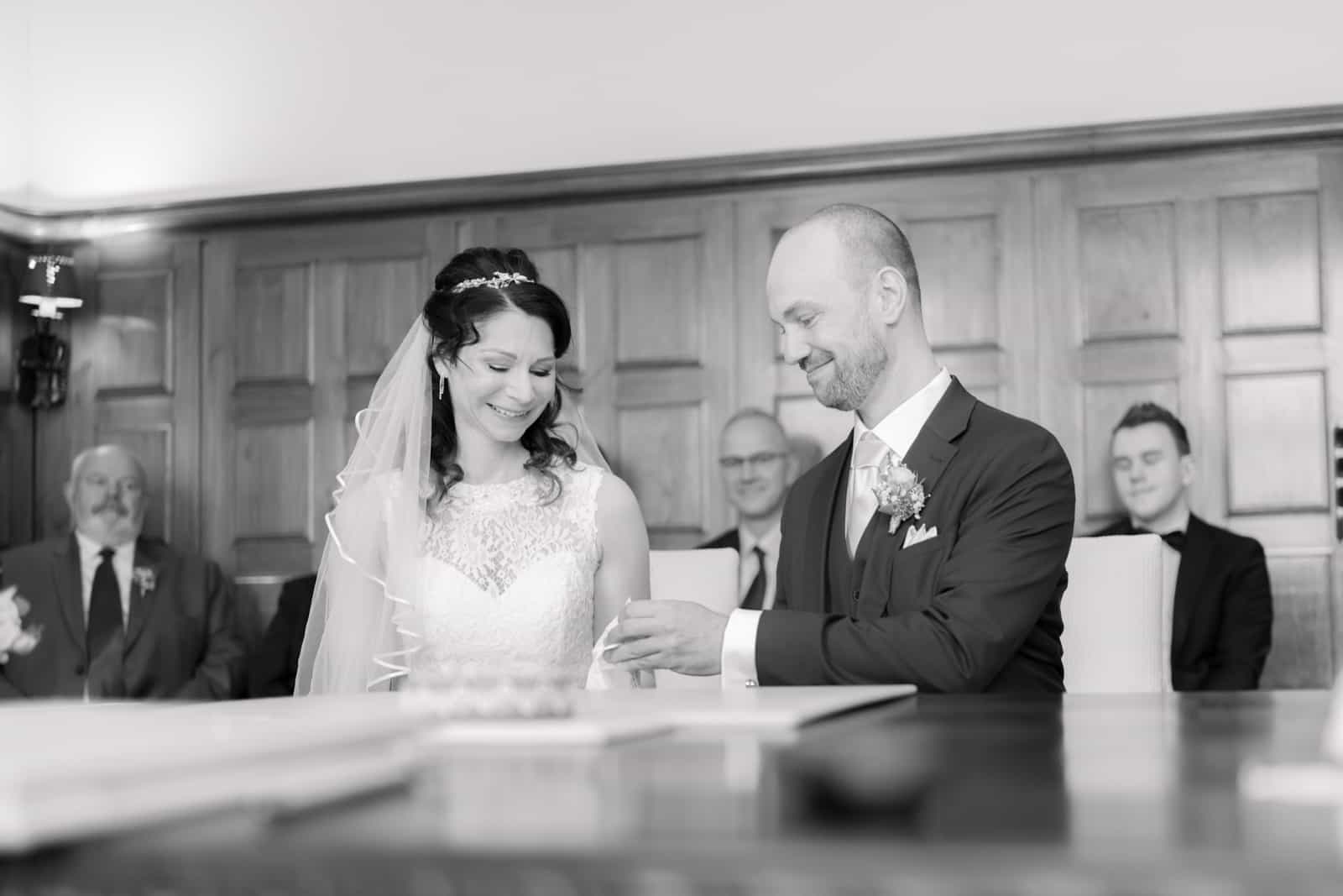 Groom placing ring on bride's finger at civil ceremony, black and white