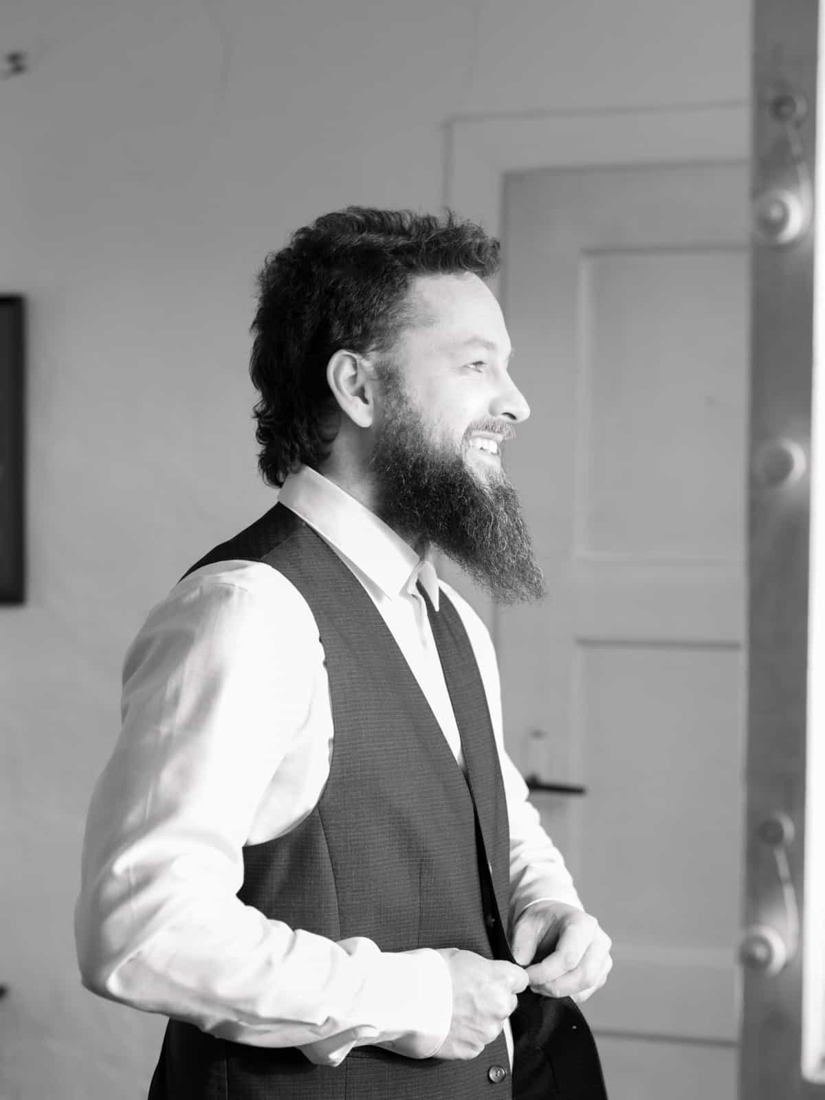 Bearded groom in blue vest by bright window