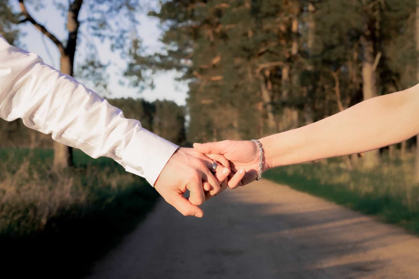 Interlocked hands with wedding rings and bracelet at golden hour