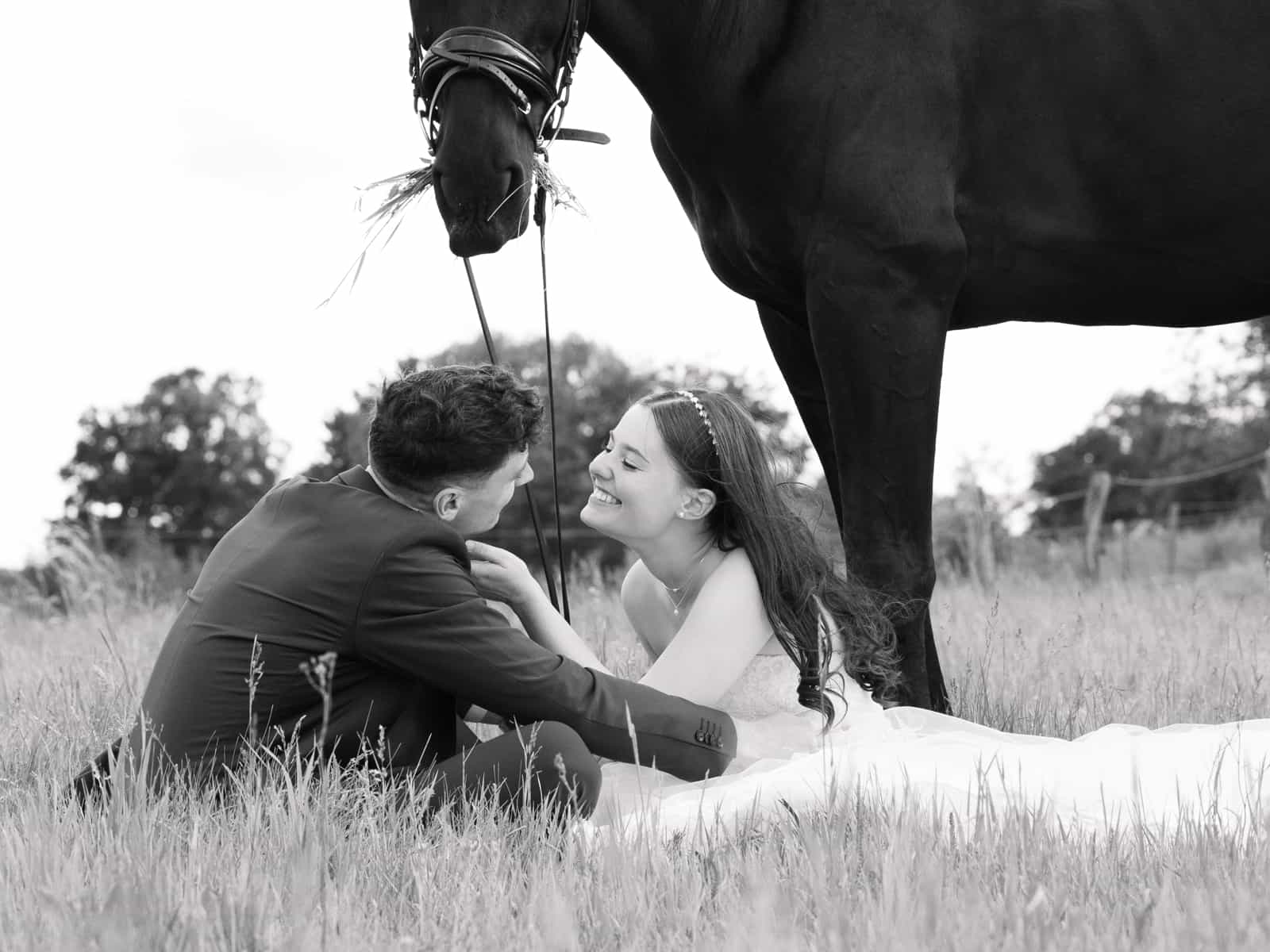Groom tenderly kissing bride's forehead under black horse's head
