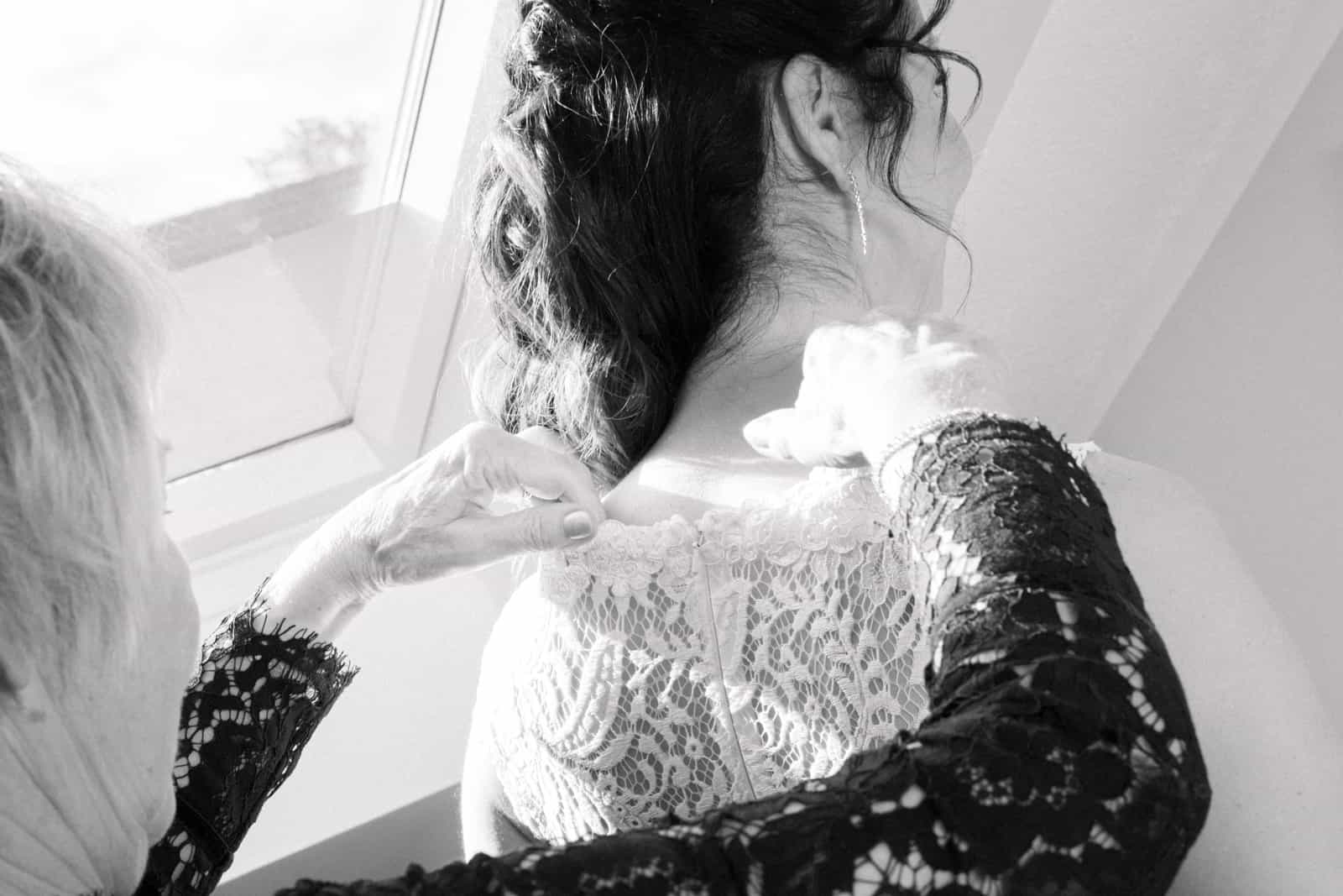Mother fastening lace wedding dress photographed from above, black and white
