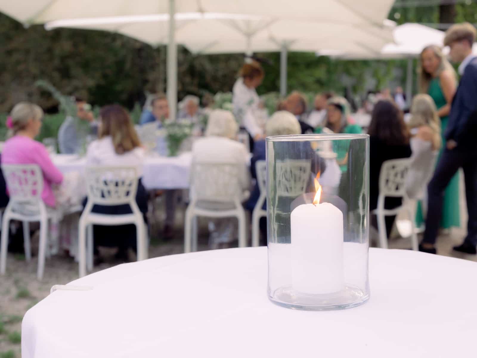 Candle in glass with blurred wedding guests in garden - outdoor wedding at Schloss Kartzow