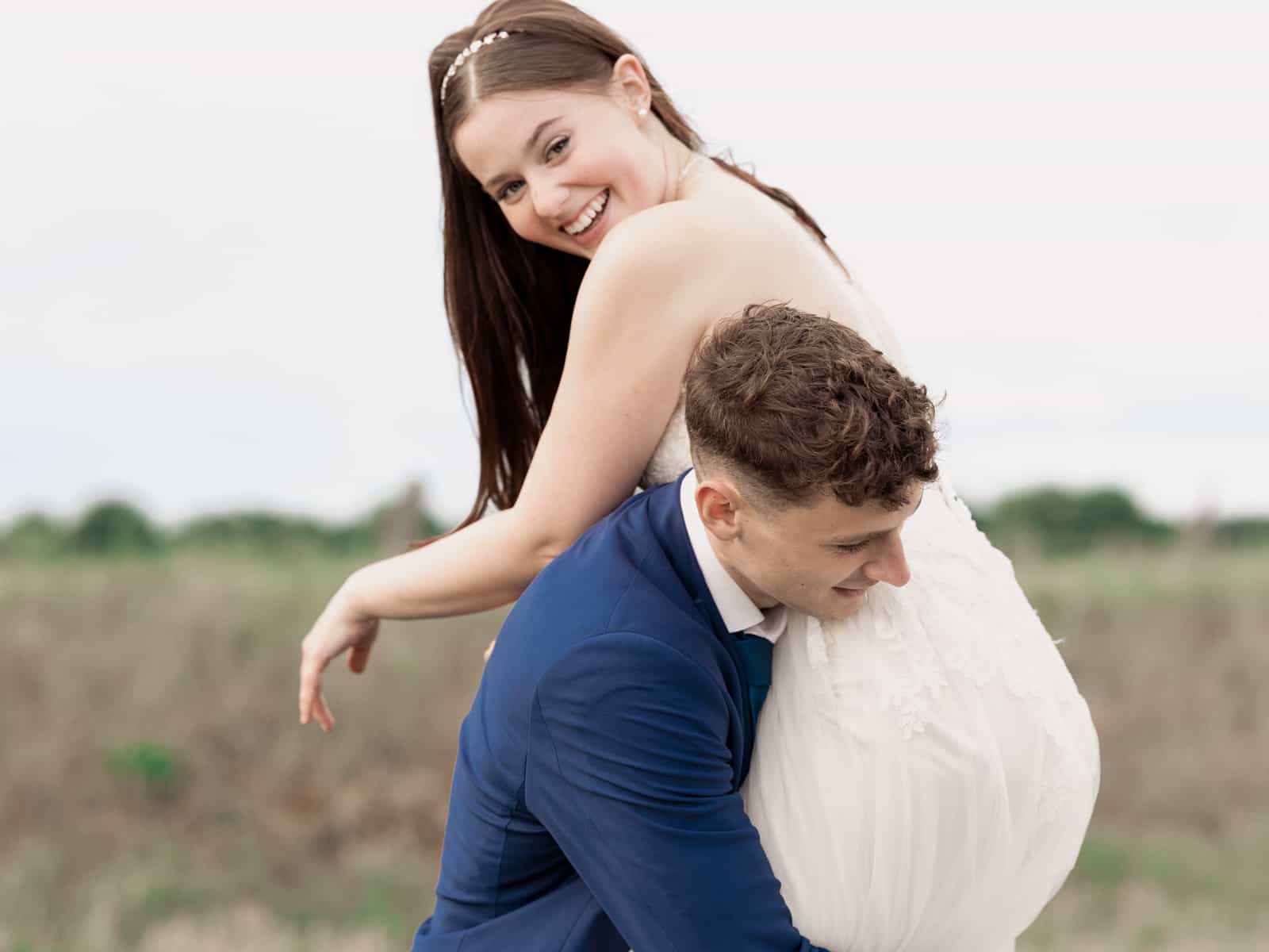 Laughing bride on groom's back on field path