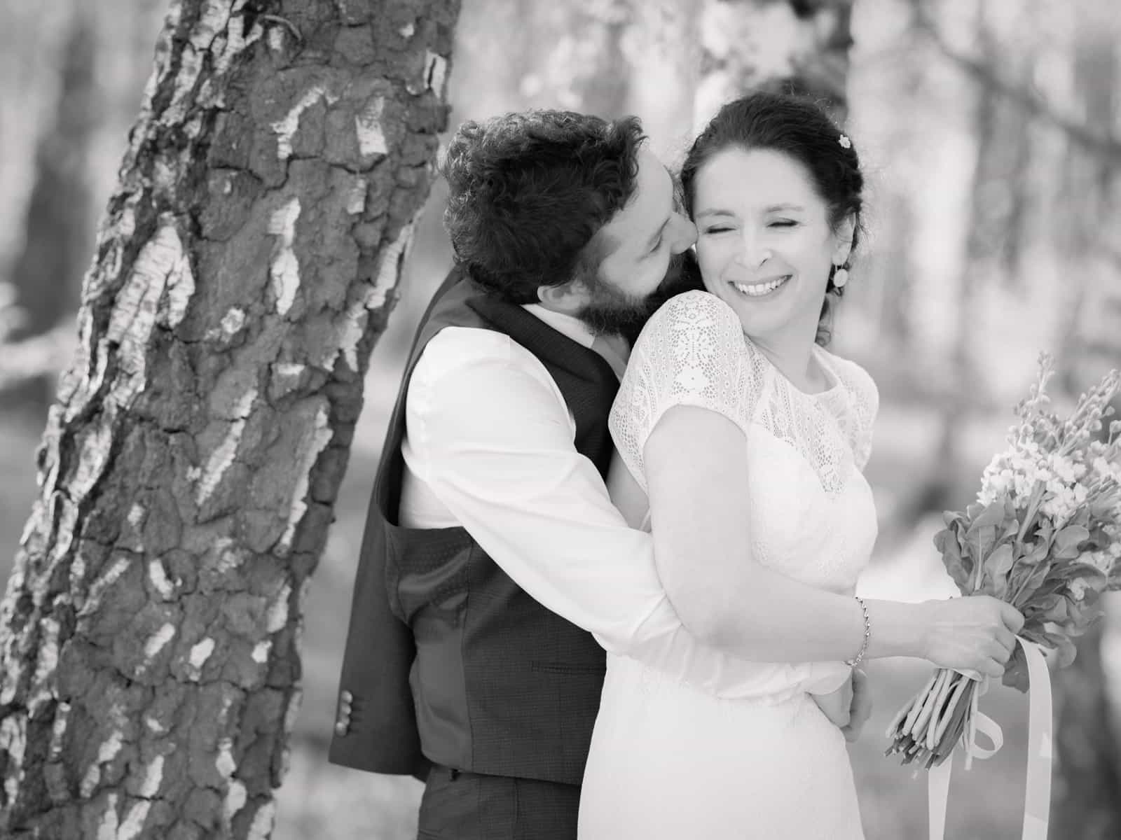 Radiant bride with flower bouquet receiving kiss from groom