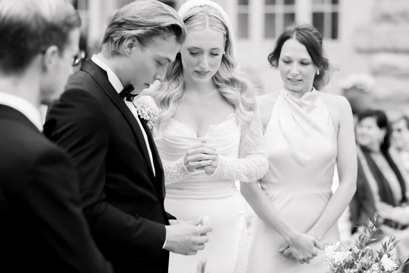 Couple exchanging rings during wedding ceremony with witness, black and white