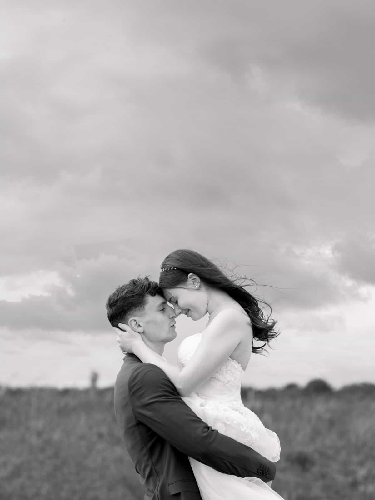 Groom lifting bride in romantic embrace on rural field path