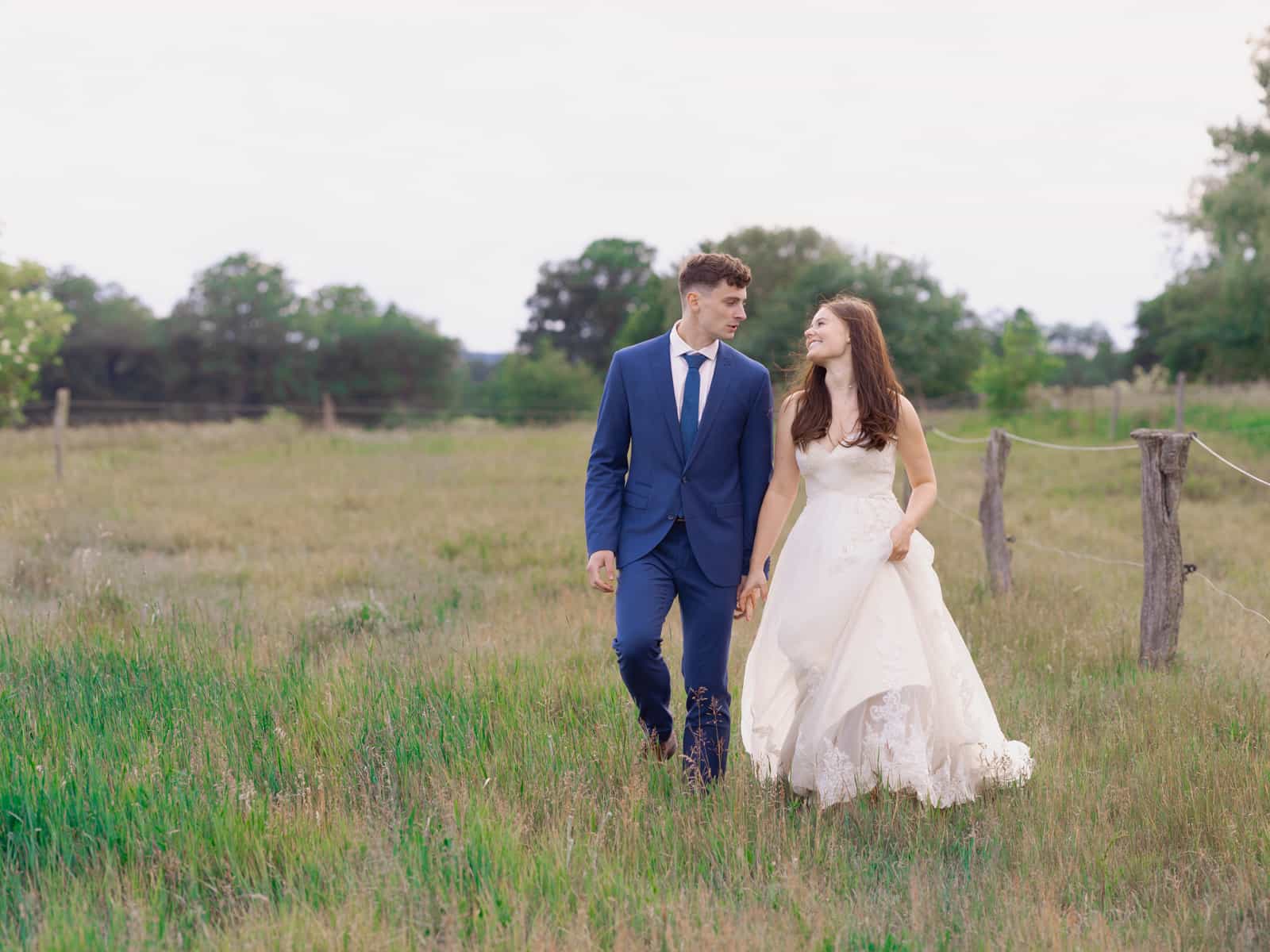 Couple walking hand in hand on field path with pasture fence