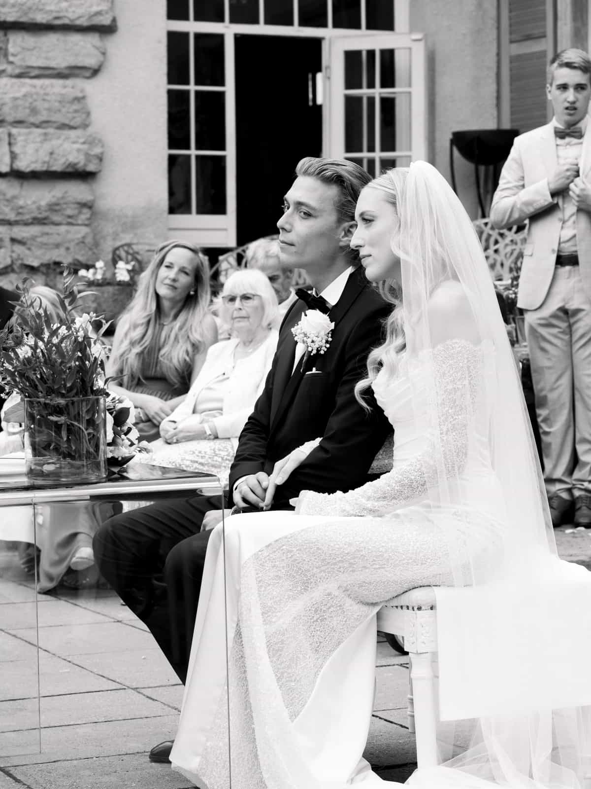 Wedding couple seated during wedding ceremony at Schloss Kartzow with guests in background