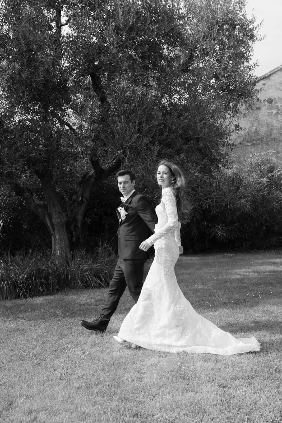Wedding couple walking through olive grove, bride in long dress with train