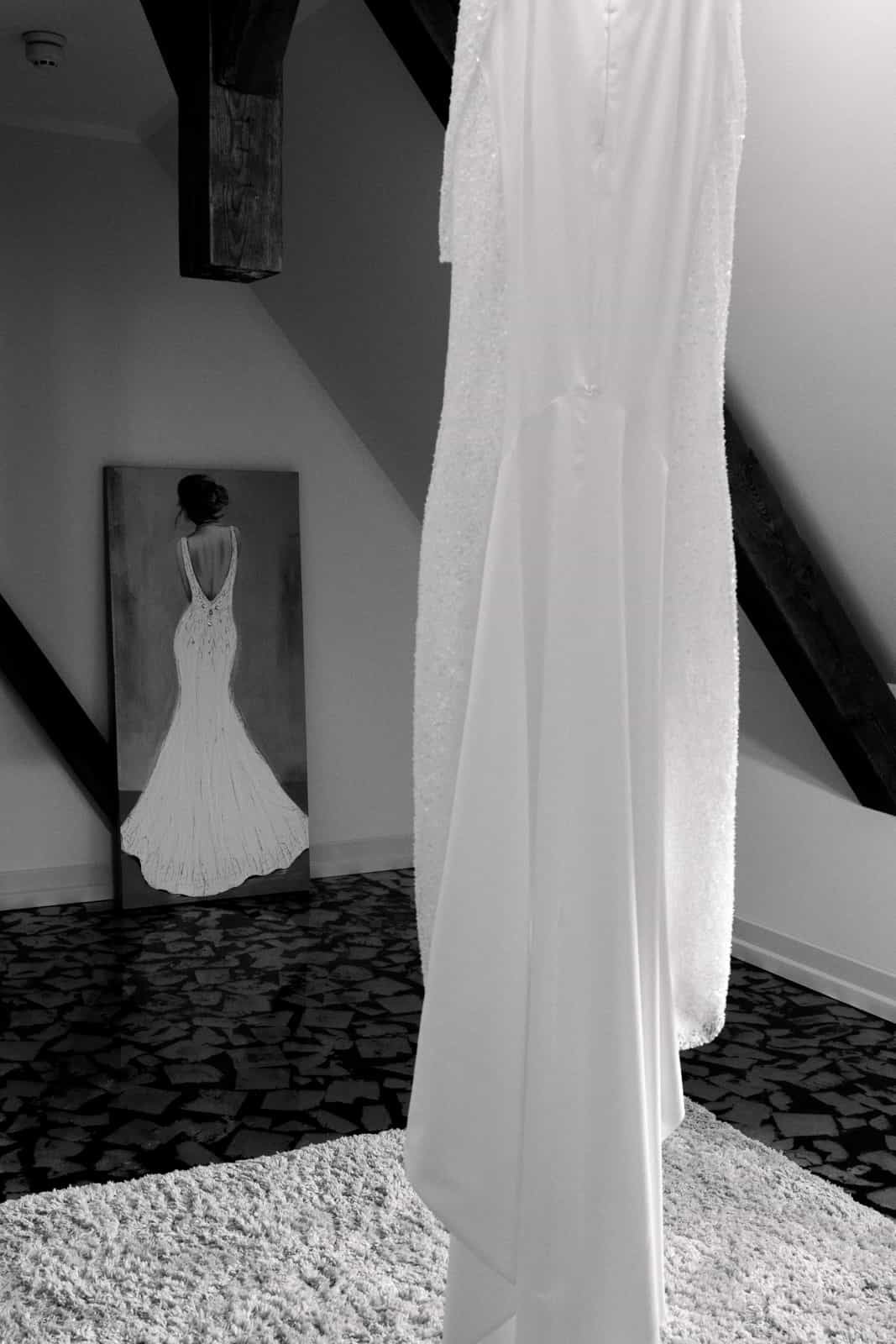 Elegant wedding dress with sleeves hanging in attic room with wooden beams, black and white
