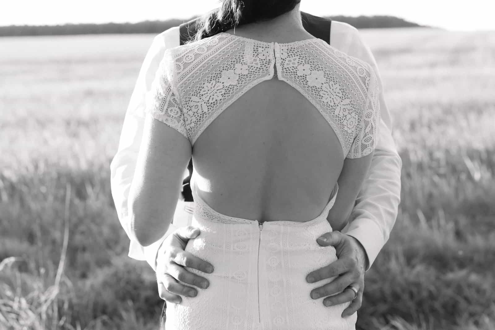 Open back wedding dress with lace, groom embracing bride from behind, black and white