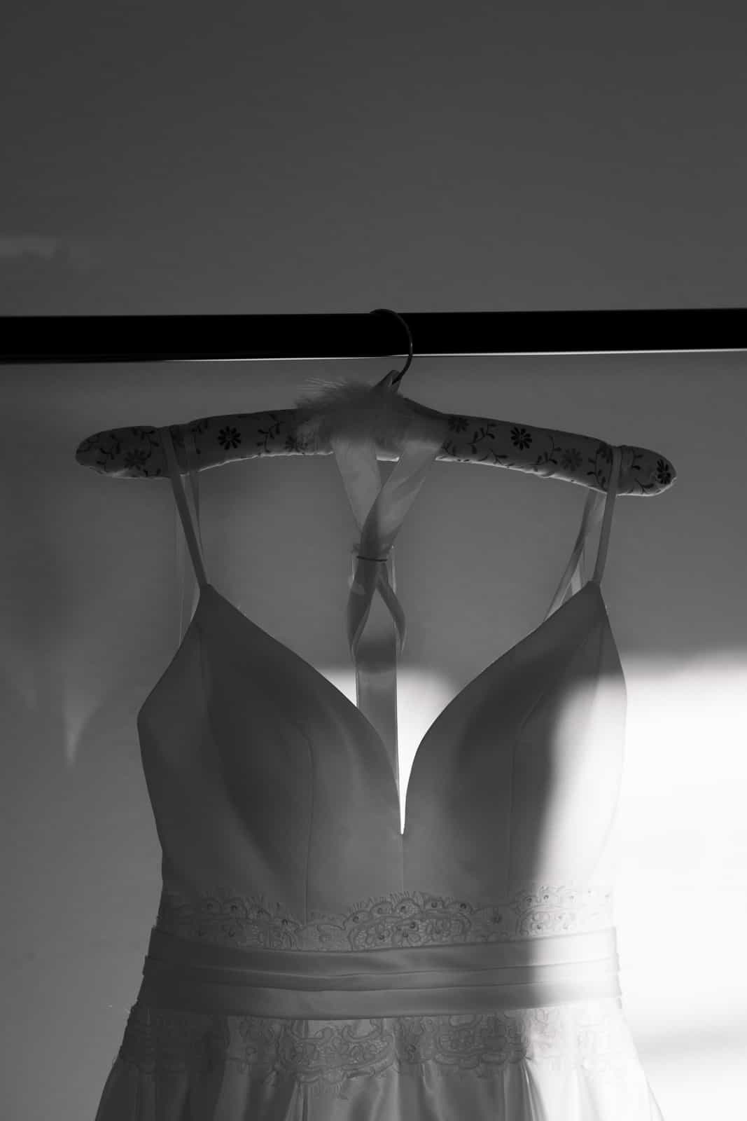 Elegant white wedding dress with lace details hanging on a floral-patterned hanger in natural light