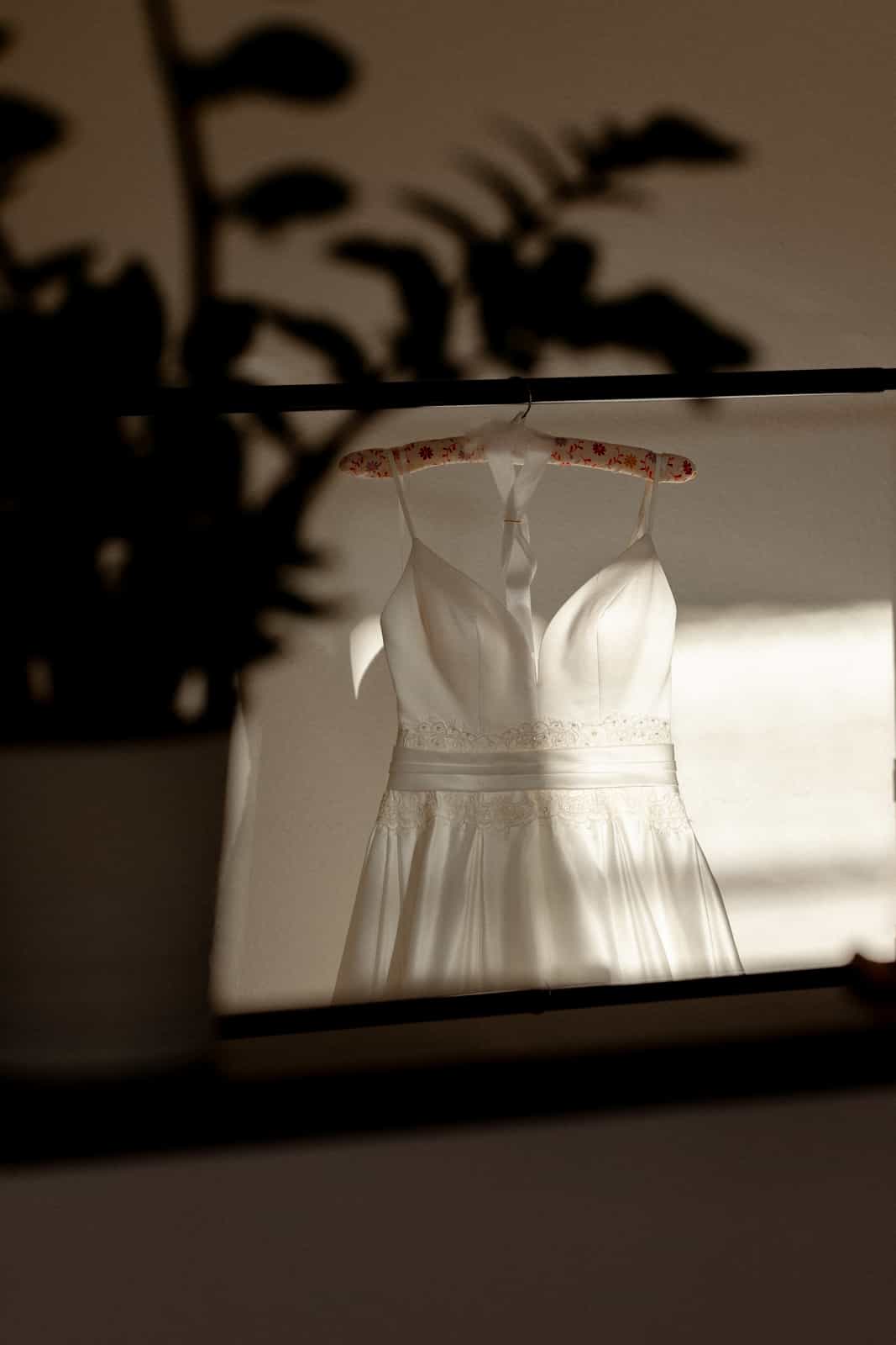 Wedding dress on floral hanger photographed through mirror with plant shadows