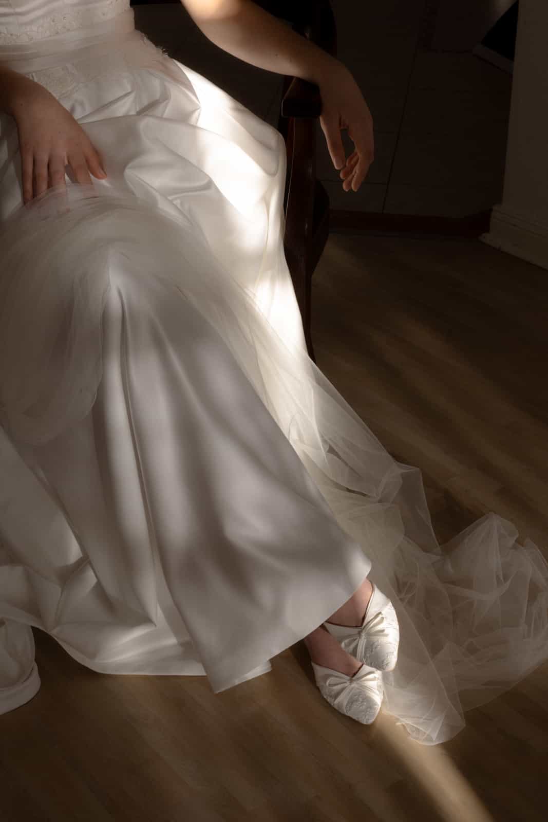 White satin wedding dress with tulle and white bridal shoes with bow during preparation